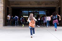 Photo of a child and her peers entering school with backpacks on